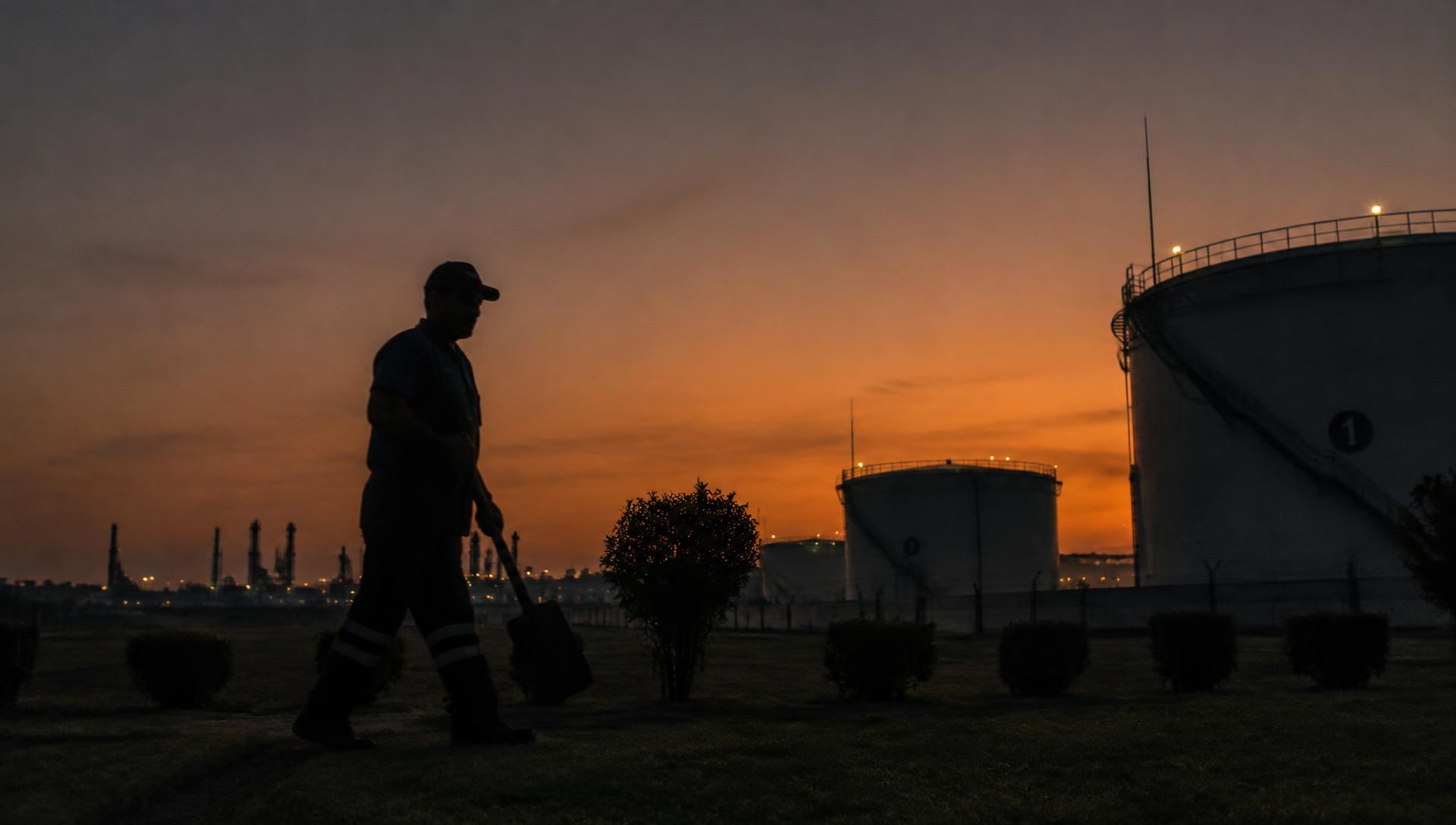 Trabajador recorriendo el perímetro de una instalación industrial al atardecer